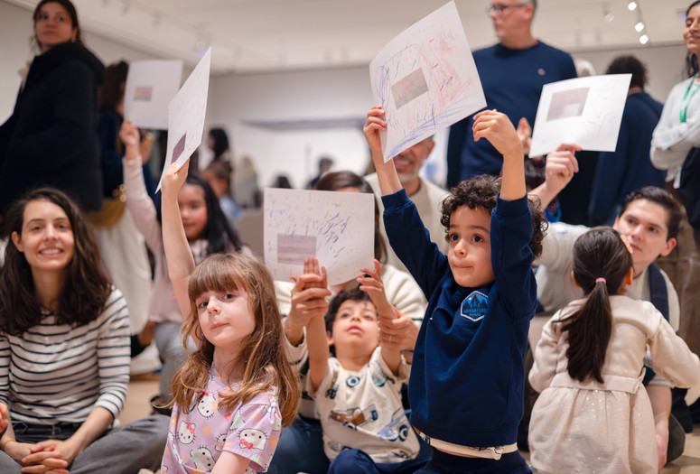 A group of children and adults hold up drawings in a gallery setting. Photo: On White Wall, Inc.