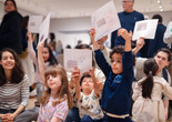 A group of children and adults hold up drawings in a gallery setting. Photo: On White Wall, Inc.