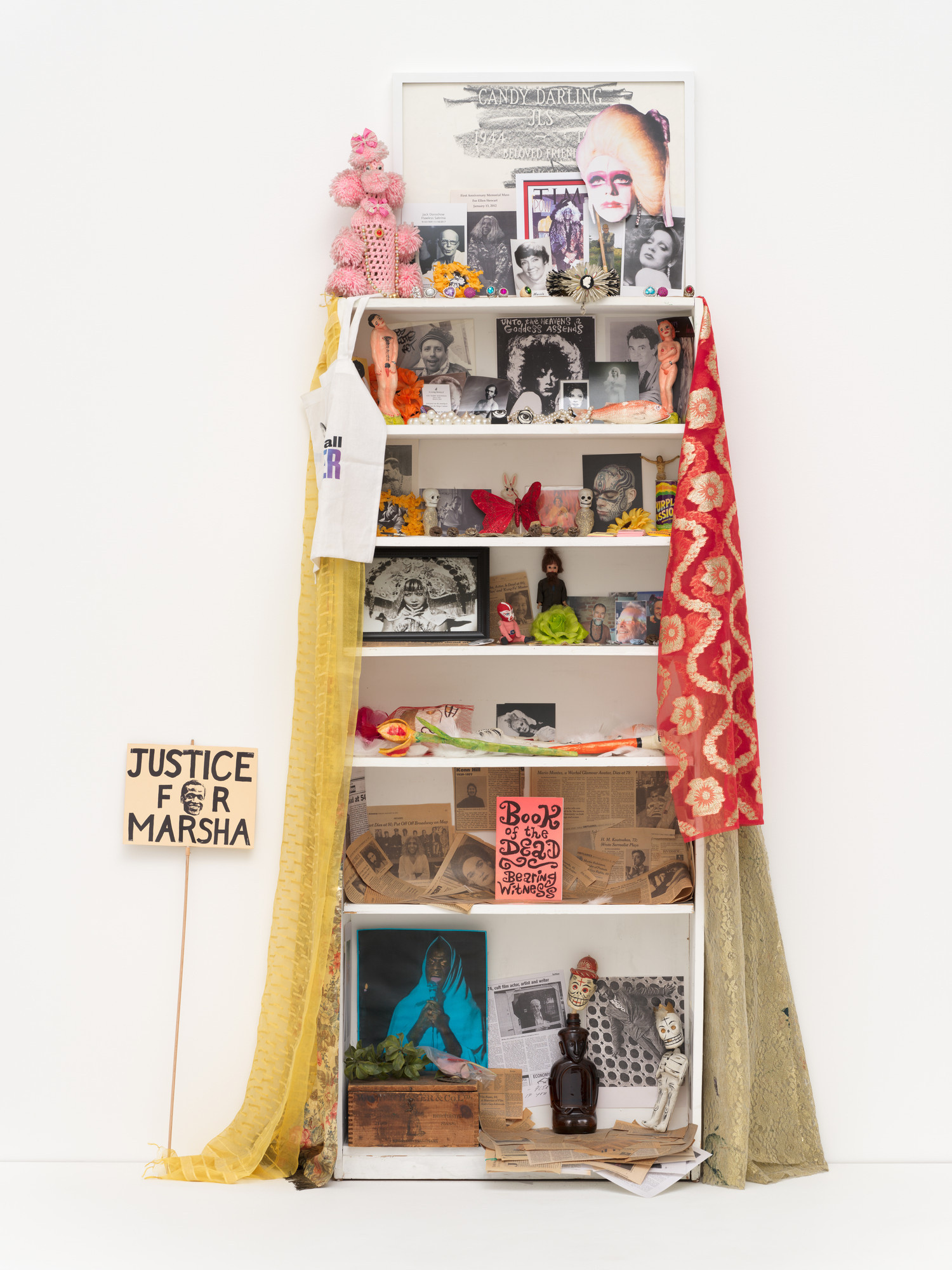 Agosto Machado. *Shrine (White)*. 2021. Mixed-media installation, with jewelry, pins, and textiles; plastic, metal, glass, and papier-mâché objects; photographs, postcards, paper mask, protest sign, memorial-service cards and programs, and newspaper and magazine clippings; and original artworks by Scott Covert, Ken Angel Davis with CAConrad, and Gene Fedorko with Stephen Tashjian (Tabboo!), 91 1/2 × 36 × 10" (232.4 × 91.4 × 25.4 cm). Acquired through the generosity of Scott Lorinsky. © 2026 Agosto Machado. Courtesy of the artist