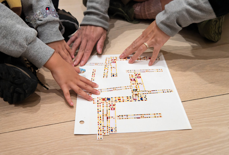 A child and adult work together on an art-making activity inspired by Broadway Boogie Woogie by Piet Mondrian on the floor of a gallery. Photo: On White Wall, Inc.
