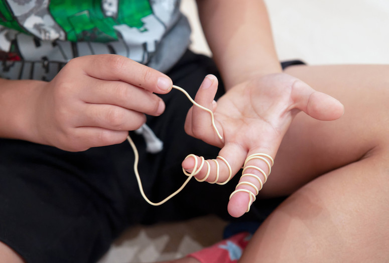 A child holds out their left hand and wraps yellow wire around it with their right hand. Photo: Martin Seck