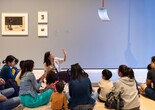 An educator leads a discussion with families in front of a sculpture of a shovel hung from the ceiling. Photo: On White Wall, Inc.