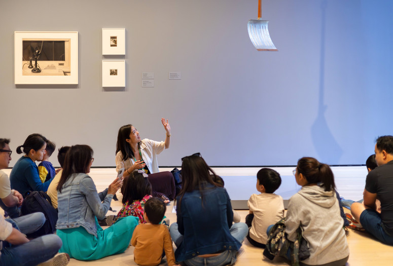 An educator leads a discussion with families in front of a sculpture of a shovel hung from the ceiling. Photo: On White Wall, Inc.