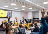 An educator sits in front of families and invites them to wave their arms in the air during Family Story Time. Photo: On White Wall, Inc.