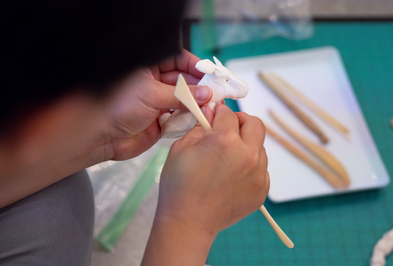 A child works on sculpting an animal out of white air-dry clay and tan-colored clay tools. Photo: On White Wall, Inc.