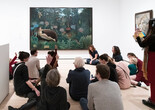 An educator leads a discussion with families in front of a painting featuring a nude woman and a tiger in a jungle. Photo: Martin Seck