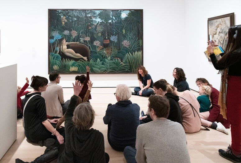 An educator leads a discussion with families in front of a painting featuring a nude woman and a tiger in a jungle. Photo: Martin Seck