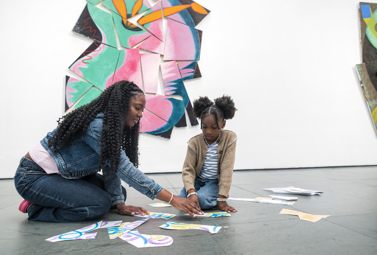 A child and adult sit in front of an artwork arranging cutout shapes.