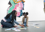 A child and adult sit in front of an artwork arranging cutout shapes.