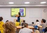 An educator stands in front of families and holds up a picture book. Photo: On White Wall, Inc.