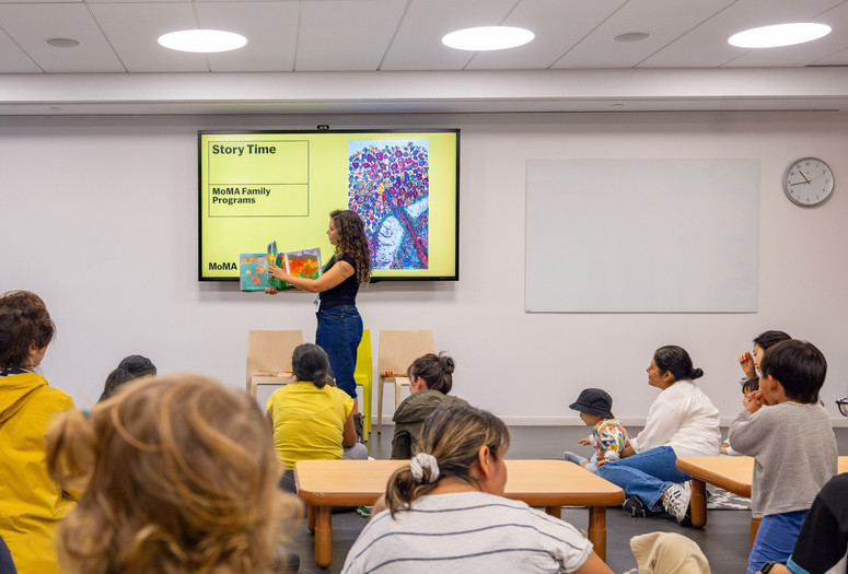 An educator stands in front of families and holds up a picture book. Photo: On White Wall, Inc.