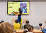 An educator stands in front of families and holds up a picture book. Photo: On White Wall, Inc.