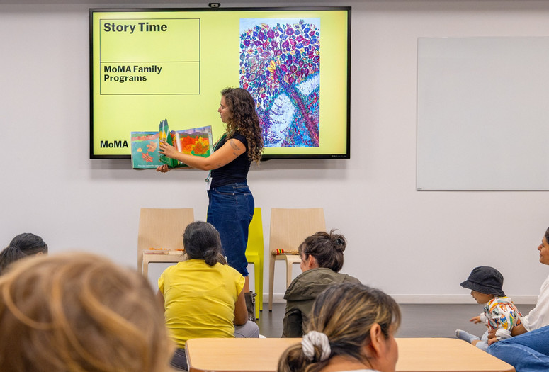 An educator stands in front of families and holds up a picture book. Photo: On White Wall, Inc.