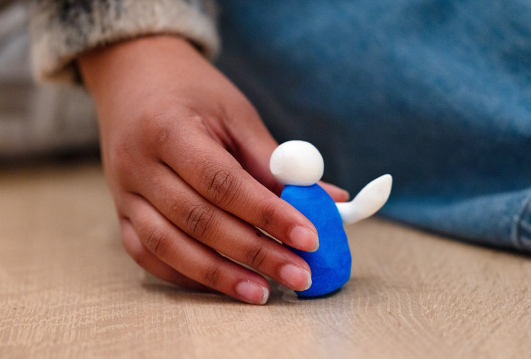 A hand holds up a figure made of air-dry clay in a gallery. Photo: On White Wall, Inc.