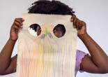 A child holds up a piece of canvas with a colorful drawing in front of their face with two holes cut into it. Photo: On White Wall, Inc.