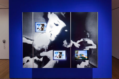 Dara Birnbaum. <i>PM Magazine</i> (detail). 1982. Four-channel video (color, three channels of stereo sound, 6:30 min.), two chromogenic prints, Speed Rail® structural support system, aluminum trim, one wall painted Chroma Key Blue, and one wall painted red, dimensions variable. Installation view, <i>Cut to Swipe</i>, The Museum of Modern Art, New York, October 11, 2014–March 22, 2015. The Museum of Modern Art, New York. Acquired with support from The Modern Women's Fund Committee, The Contemporary Arts Council of The Museum of Modern Art, and through the generosity of Ahmet Kocabiyik, 2014. © 2015 Dara Birnbaum. Image courtesy the artist and Marian Goodman Gallery, New York and Paris