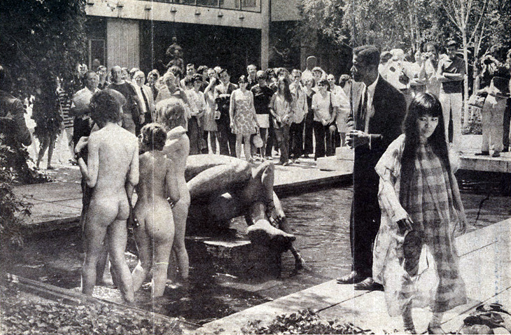 Photo of Yayoi Kusama’s “Grand Orgy to Awaken the Dead.” An audience looks on as several naked people stand next to a statue in one of the pools in the garden