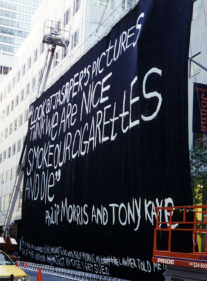 Photo of an immense canvas painted with the words “LOOK AT JASPER’s PICTURES / THINK WE ARE NICE / SMOKE OUR CIGARETTES / AND DIE,” signed PHILIP MORRIS AND TONY KAYE