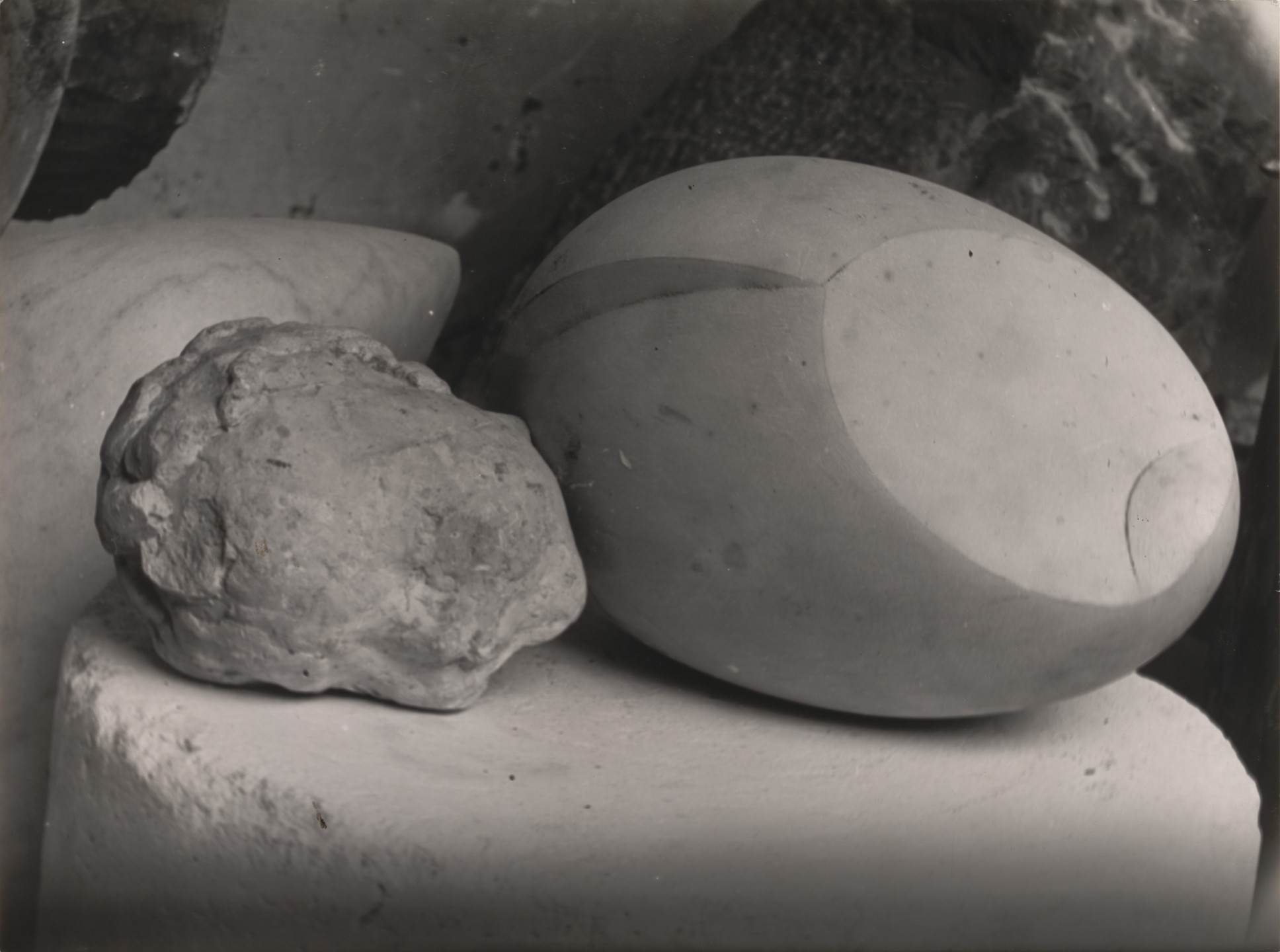 A grayscale image shows two smooth, rounded stone sculptures placed side by side on a pedestal. The left piece is irregular with rugged textures, while the right one is oval and more polished. This is an AI generated description. To give feedback, email ai@moma.org.