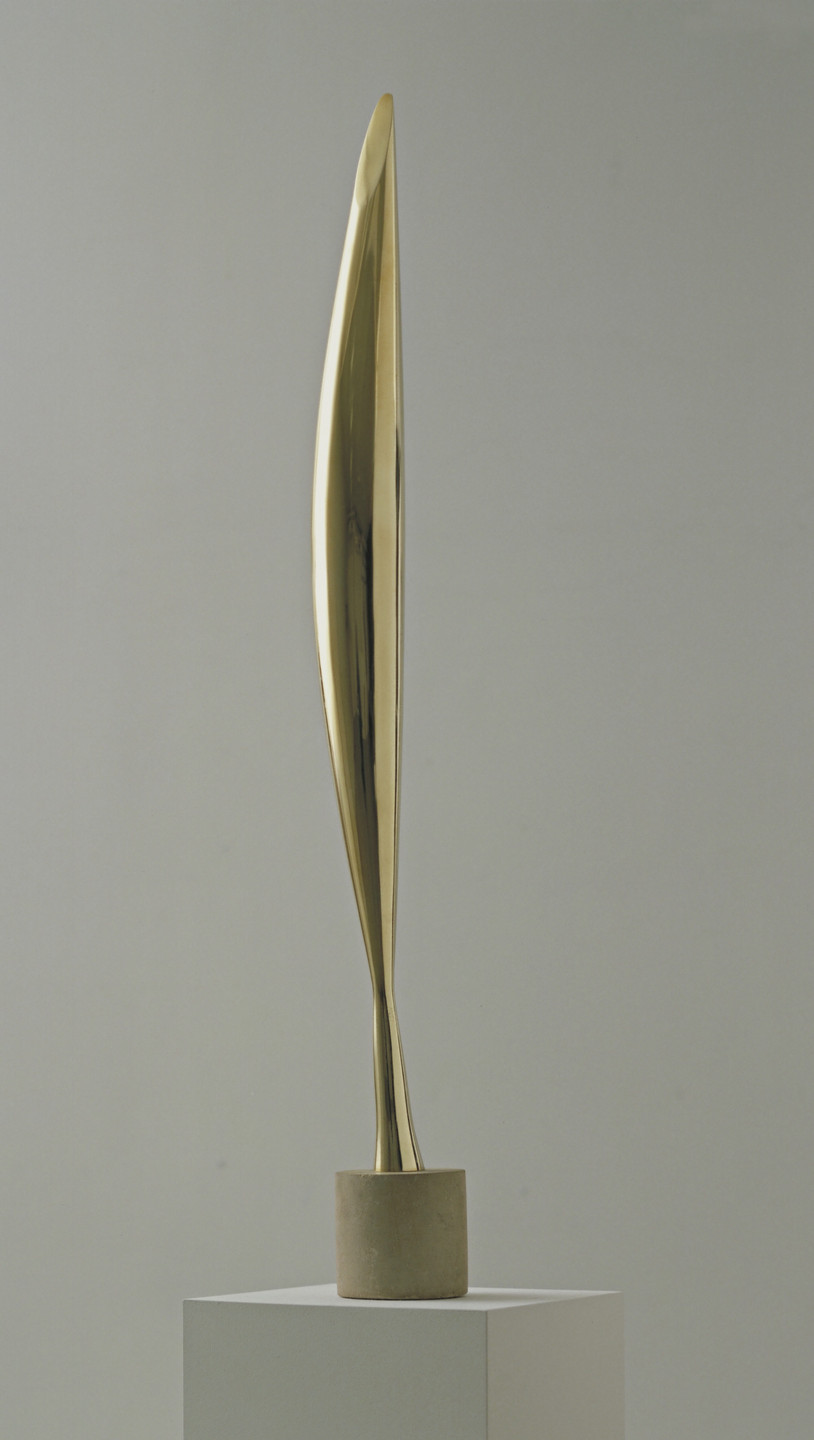 A sleek, elongated, gold-colored sculpture stands on a cylindrical stone base atop a white pedestal. The sculpture narrows towards the top, with gentle curves and a smooth, reflective surface. This is an AI generated description. To give feedback, email ai@moma.org.