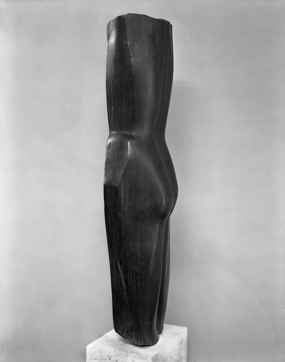 A smooth, black, vertical sculpture resembling the lower half of a human torso and legs stands on a white rectangular base against a plain light gray background. It has rounded contours and a polished surface. This is an AI generated description. To give feedback, email ai@moma.org.