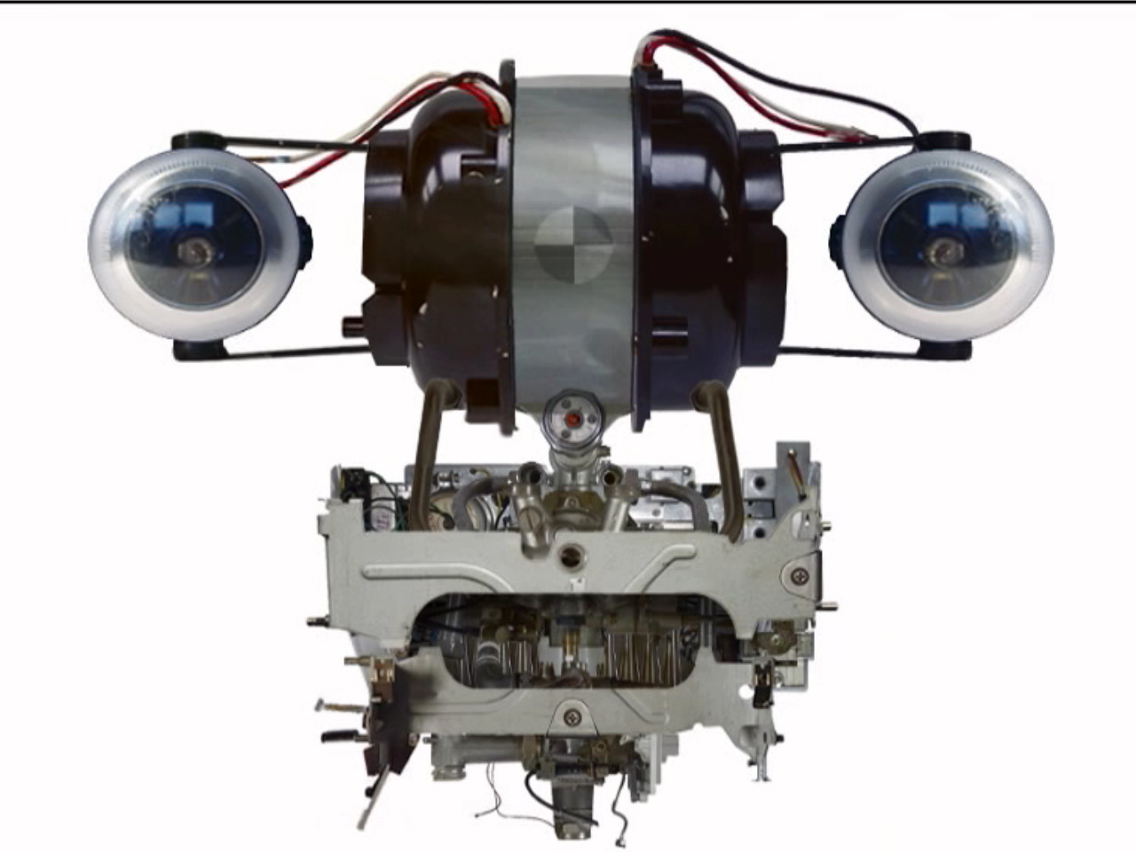 The image depicts a mechanical object with two round, blue and silver components at the top, resembling eyes. Below, a complex arrangement of metallic parts and wires is visible, primarily in silver and gray tones. This is an AI generated description. To give feedback, email ai@moma.org.