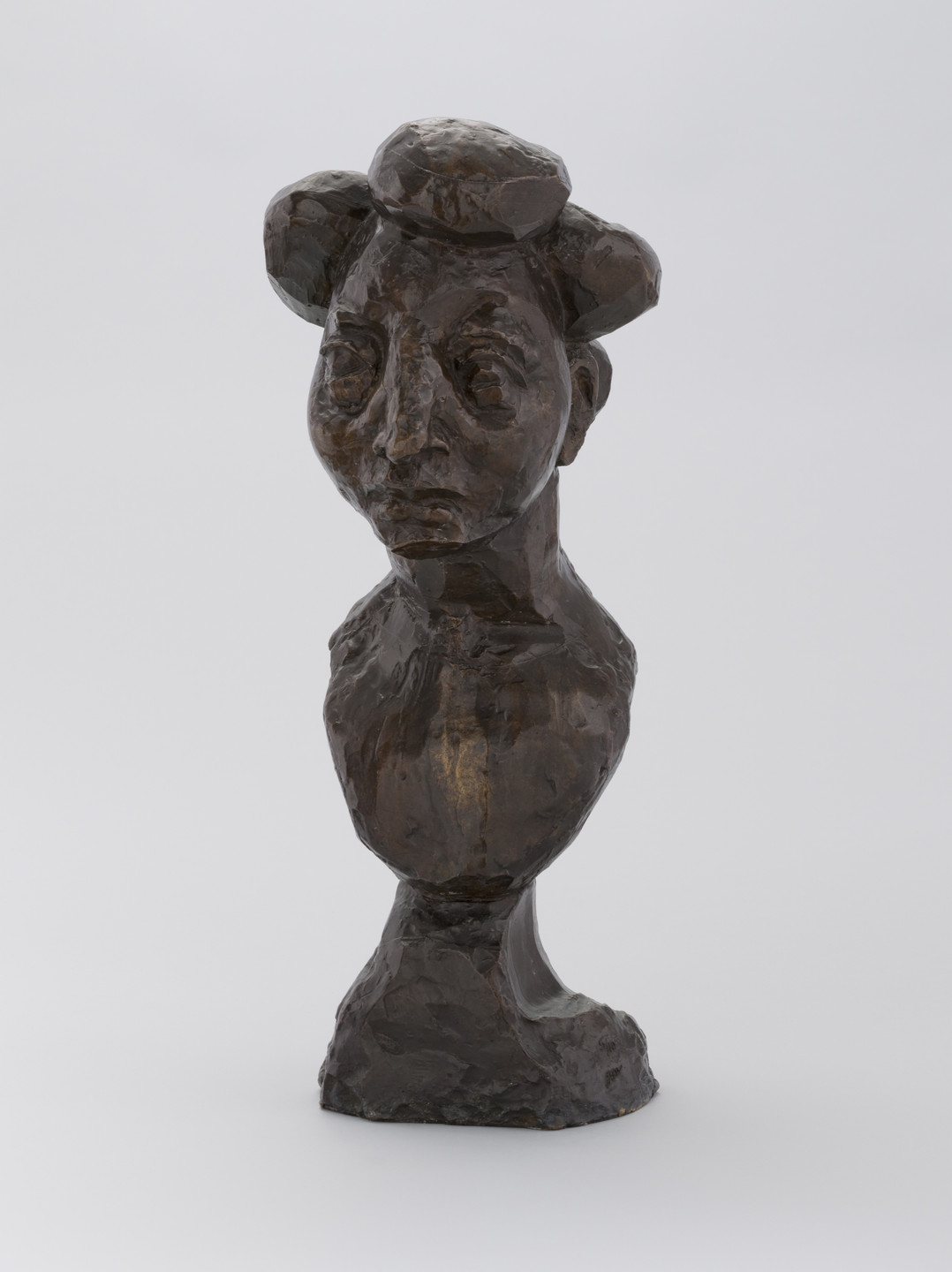 A dark bronze sculpture depicting a distorted human bust with exaggerated facial features and textured surface. The figure has large, prominent ears and an elongated neck, set against a plain, light gray background. This is an AI generated description. To give feedback, email ai@moma.org.