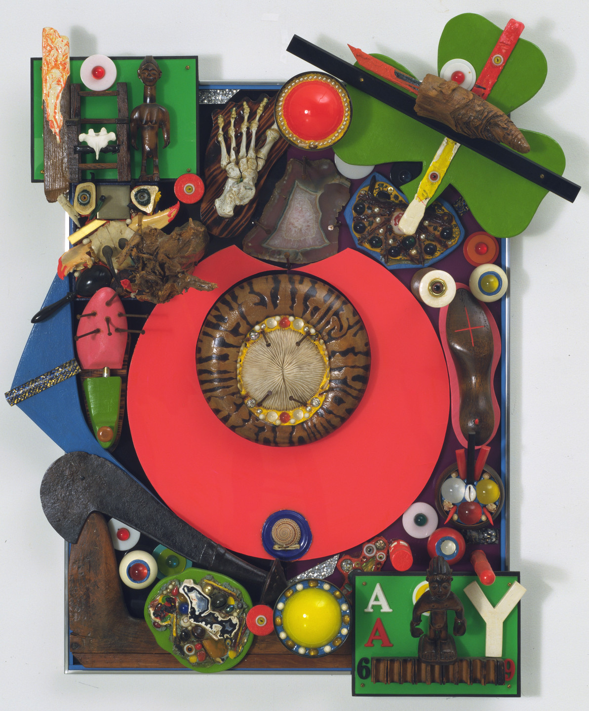 The image features a collage of various objects with predominant colors of red, green, and brown. Central elements include a large red circle, a carved wooden figure, a skeletal hand, and multiple smaller objects like buttons and beads. This is an AI generated description. To give feedback, email ai@moma.org.