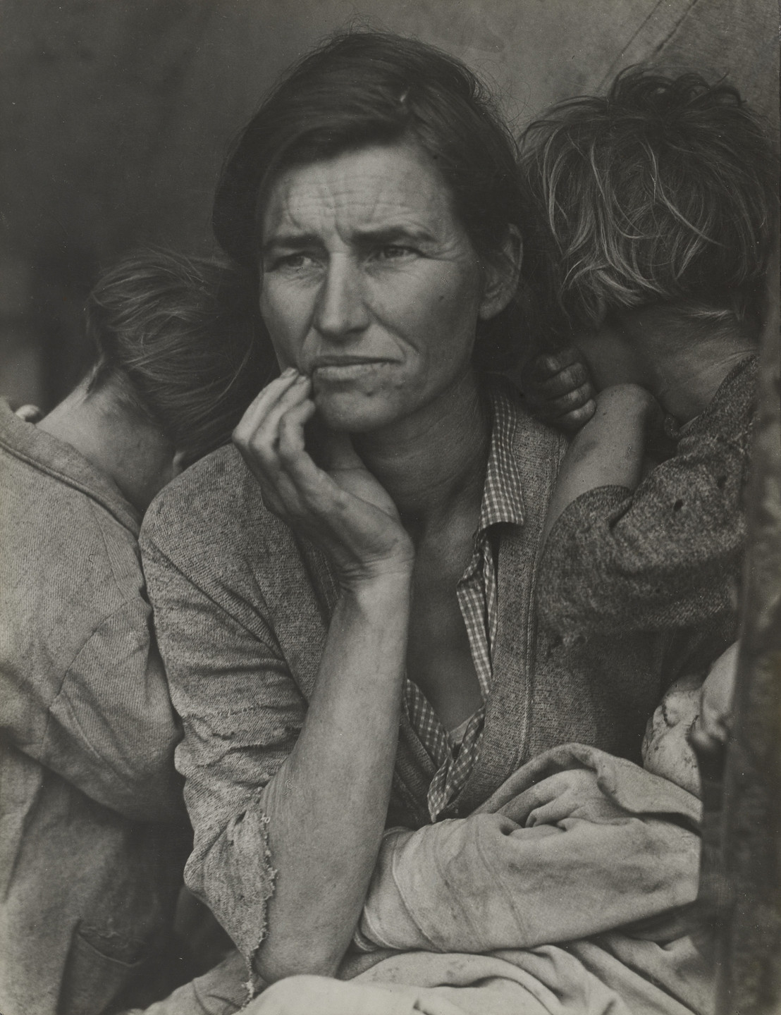 A person with weathered skin is seated with a pensive expression, resting their hand on their face. Two children with unkempt hair are leaning against them, and a baby is cradled in their lap. This is an AI generated description. To give feedback, email ai@moma.org.