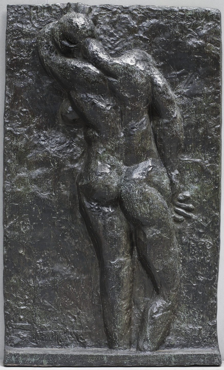 The image shows a dark, textured rectangular relief sculpture of a standing, muscular nude figure viewed from the back, with one arm raised and the other bent behind the hip. The predominant color is dark greenish bronze. This is an AI generated description. To give feedback, email ai@moma.org.