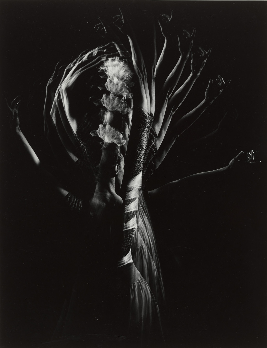 The image shows a dark figure against a black background with multiple overlapping outlines of arms and a flowing, wavy, white fabric. The predominant colors are black and grey. This is an AI generated description. To give feedback, email ai@moma.org.