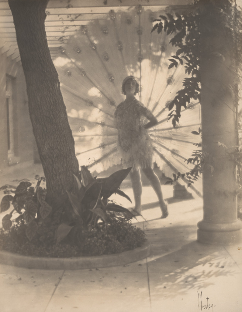 Violet Romer. (standing between tree and column with peacock fan)