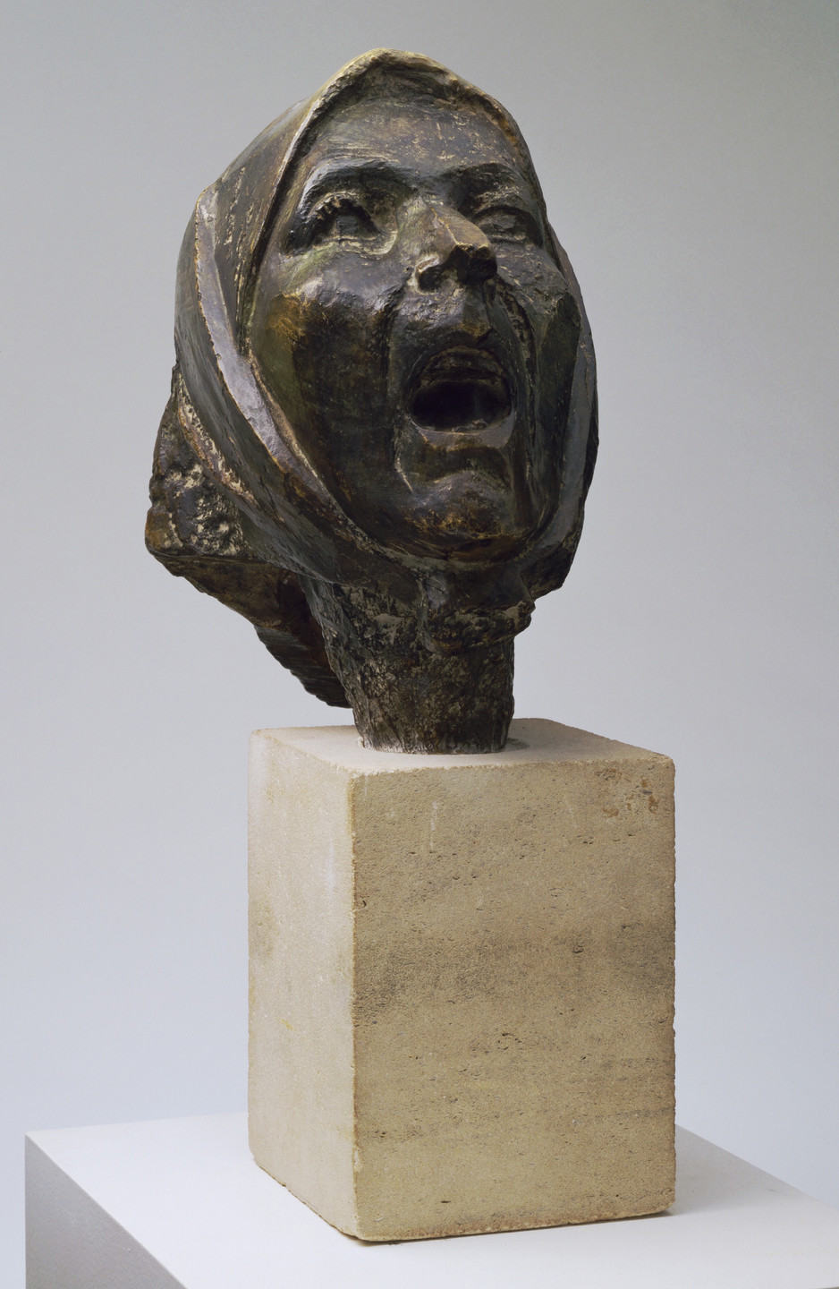 A dark bronze-colored sculpture of a person's head with their mouth open in a scream or shout, mounted on a beige pedestal. The head is draped with a textured cloth or hood. This is an AI generated description. To give feedback, email ai@moma.org.