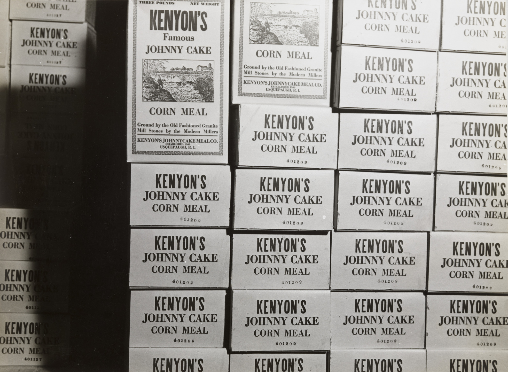 The image shows a stack of boxes labeled &#34;Kenyons Johnny Cake Corn Meal&#34; in black text on a light gray background. The predominant colors are black and gray. This is an AI generated description. To give feedback, email ai@moma.org.