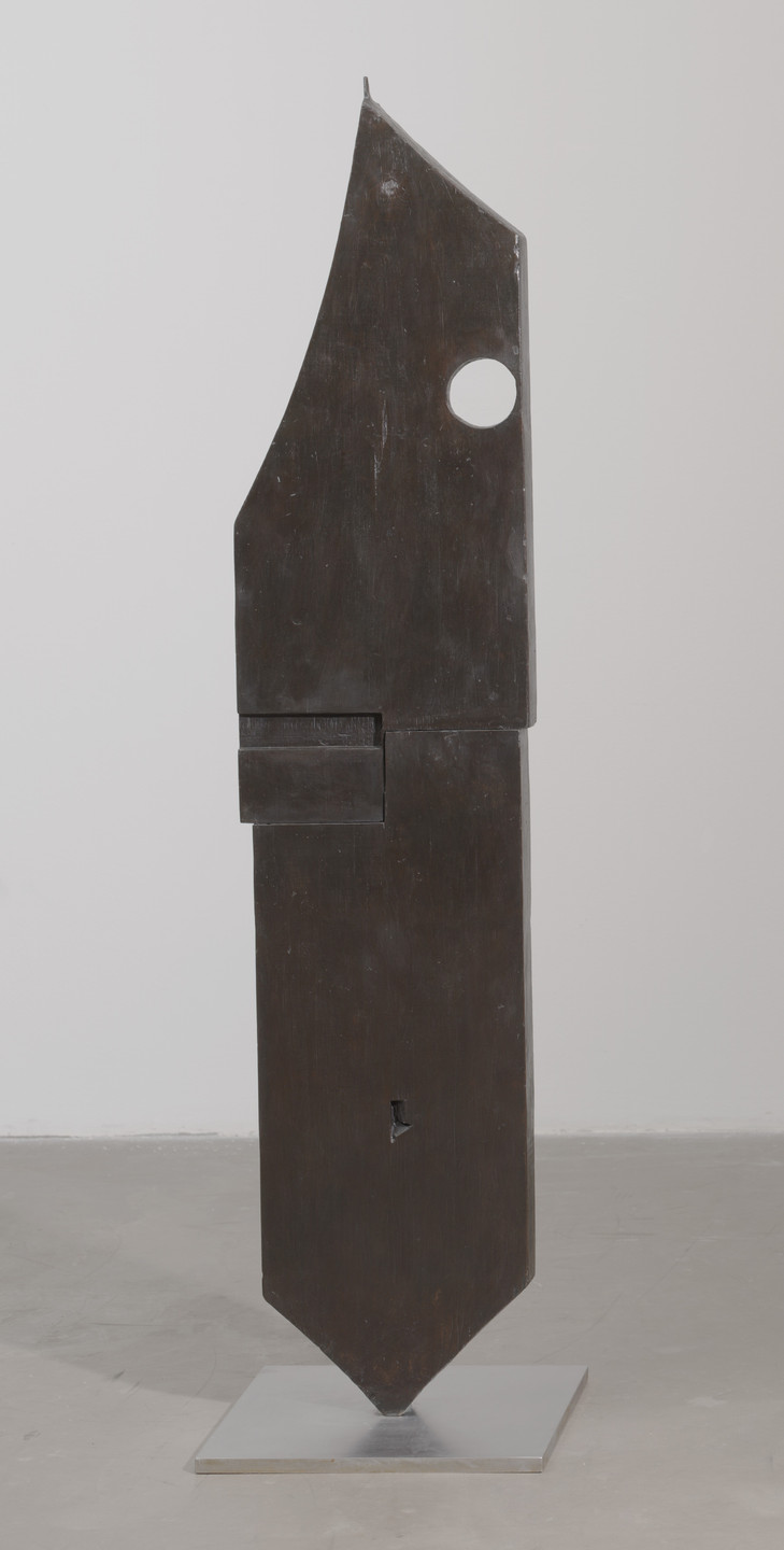 A tall, angular, dark brown sculpture stands on a gray square base. It features a large circular hole near the top and a smaller irregular hole closer to the bottom. This is an AI generated description. To give feedback, email ai@moma.org.