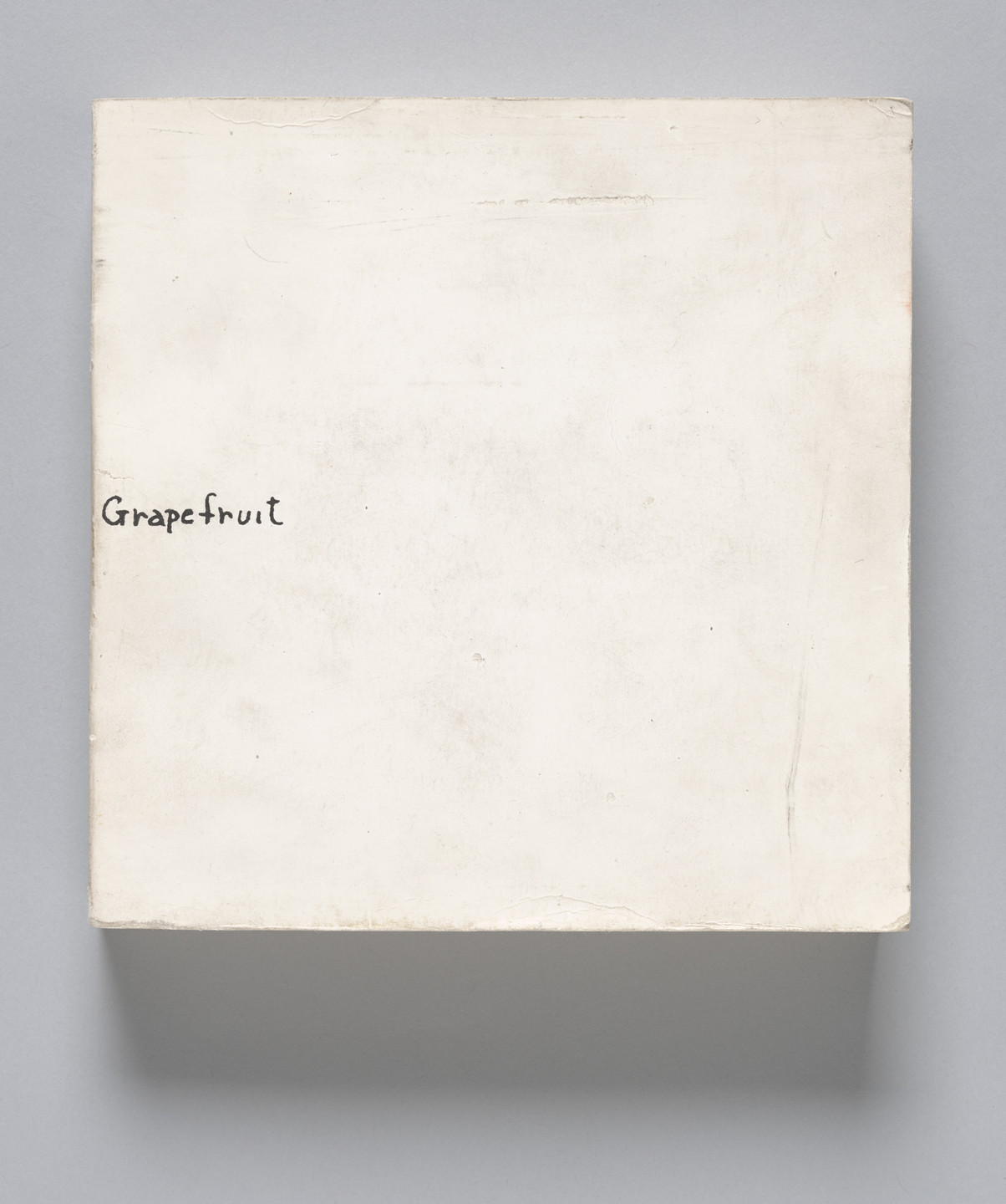 A white, slightly textured square canvas with the word &#34;Grapefruit&#34; handwritten in black ink in the lower left corner. The background is plain and evenly colored. This is an AI generated description. To give feedback, email ai@moma.org.