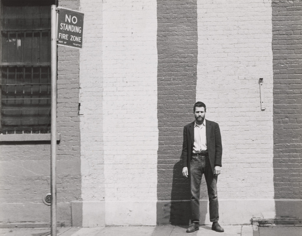 Allan Kaprow portrait in front of painted brick wall