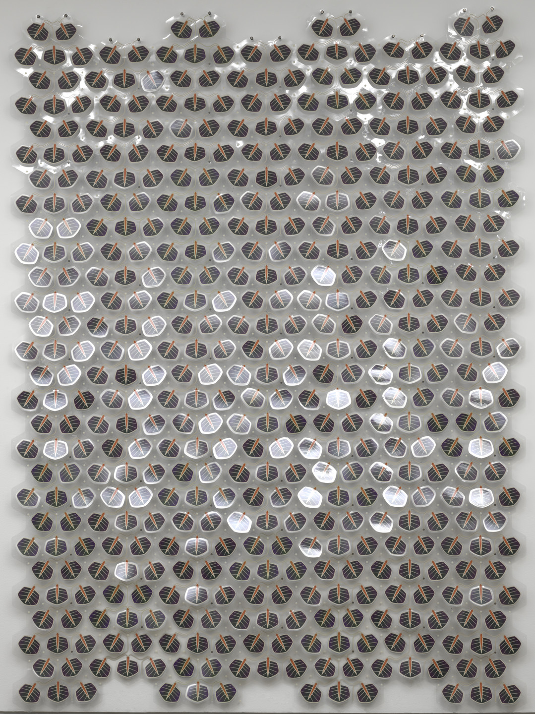 The image shows numerous metallic hexagonal tiles with reflective surfaces, arranged in a grid pattern on a light gray background. Each tile has a circular center featuring linear patterns in red, green, yellow, and blue. This is an AI generated description. To give feedback, email ai@moma.org.