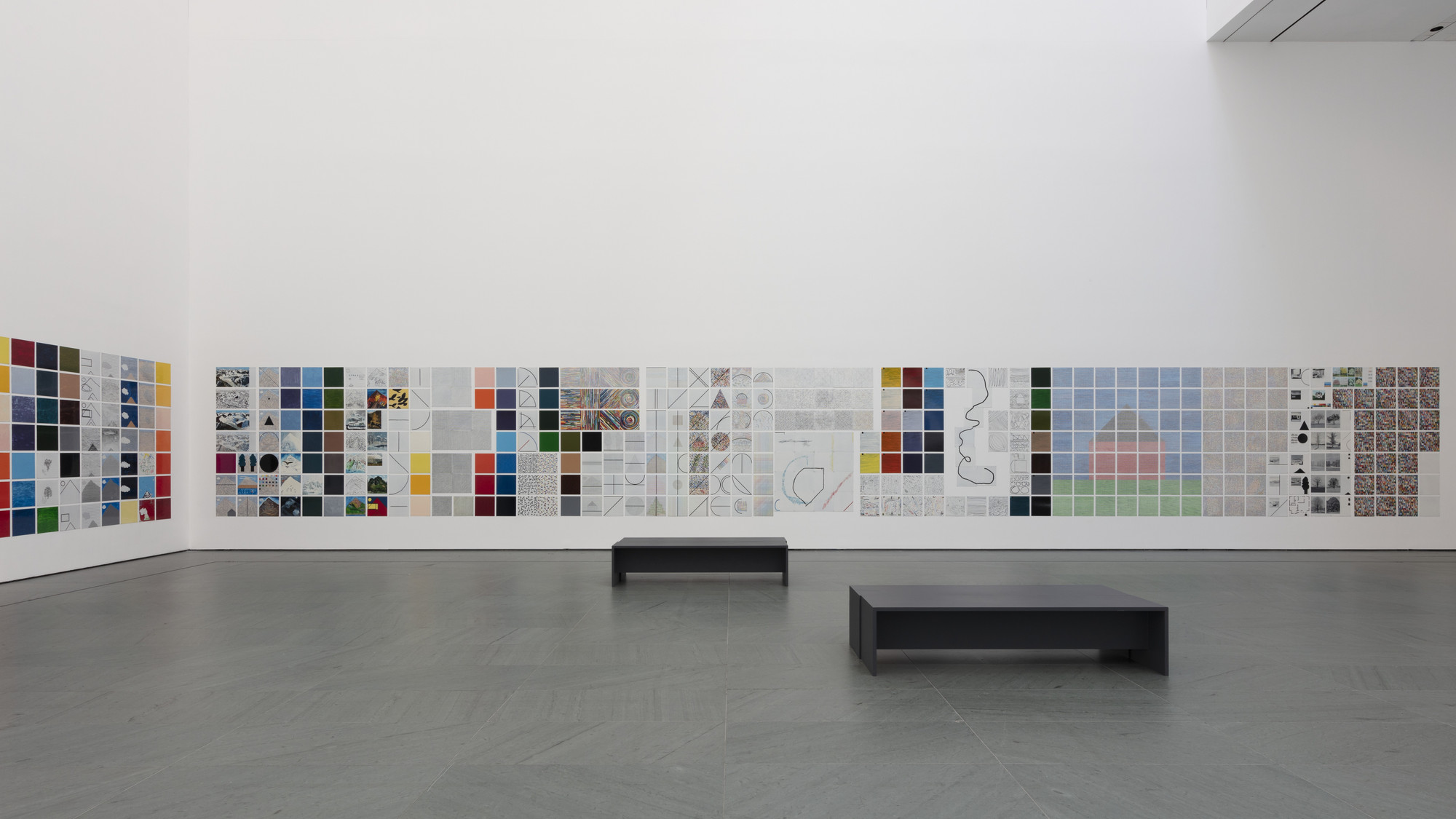 The image shows a gallery with white walls displaying a large grid of colorful and patterned squares, arranged in rows. There are two black rectangular benches on a gray floor. This is an AI generated description. To give feedback, email ai@moma.org.