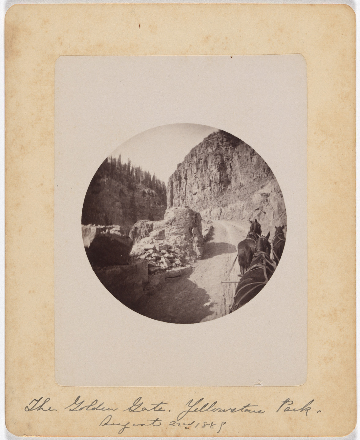 A sepia-toned photograph shows a mountainous canyon path with a horse-drawn carriage on the right side. The path is surrounded by rocky cliffs and sparse trees. This is an AI generated description. To give feedback, email ai@moma.org.