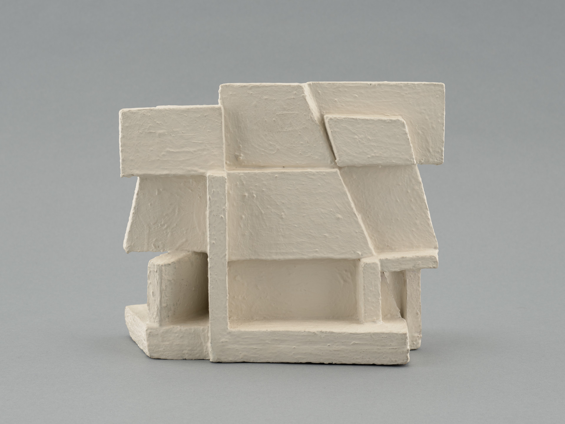 A white sculpture composed of geometric shapes, primarily squares and rectangles, with a matte finish. The background is a solid, light gray color. This is an AI generated description. To give feedback, email ai@moma.org.