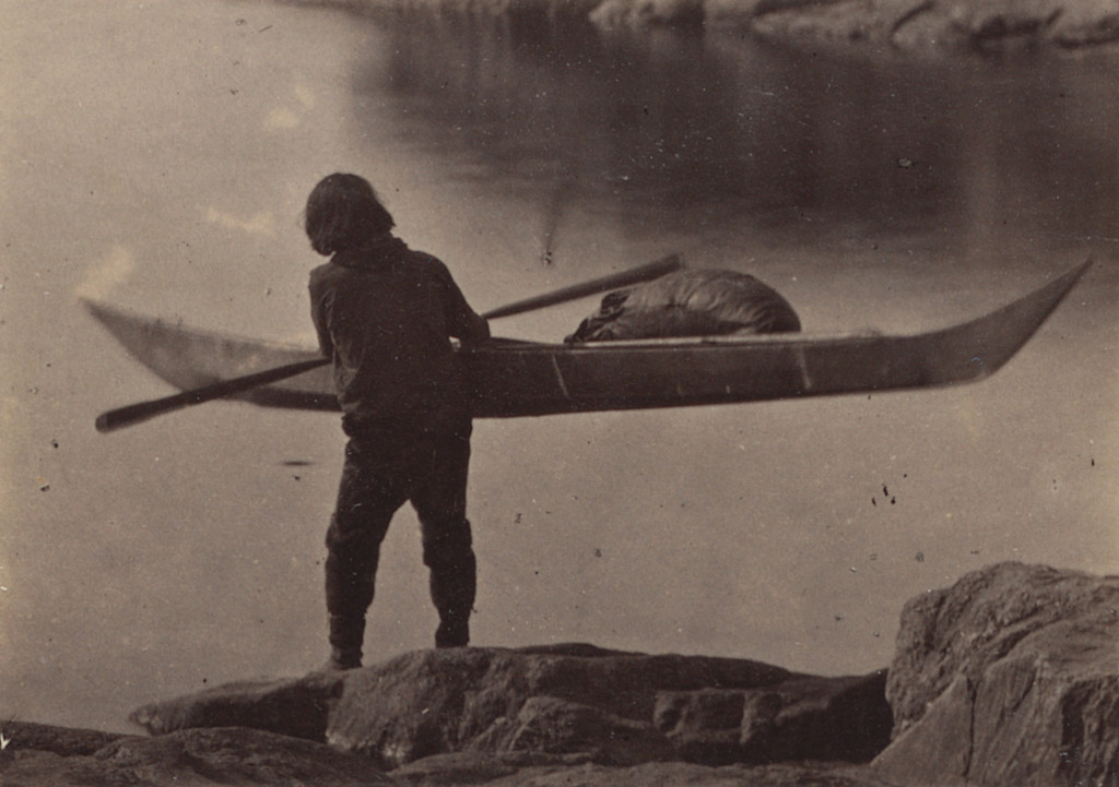 "Esquimaux carrying his kayak to the water to start on hunt"