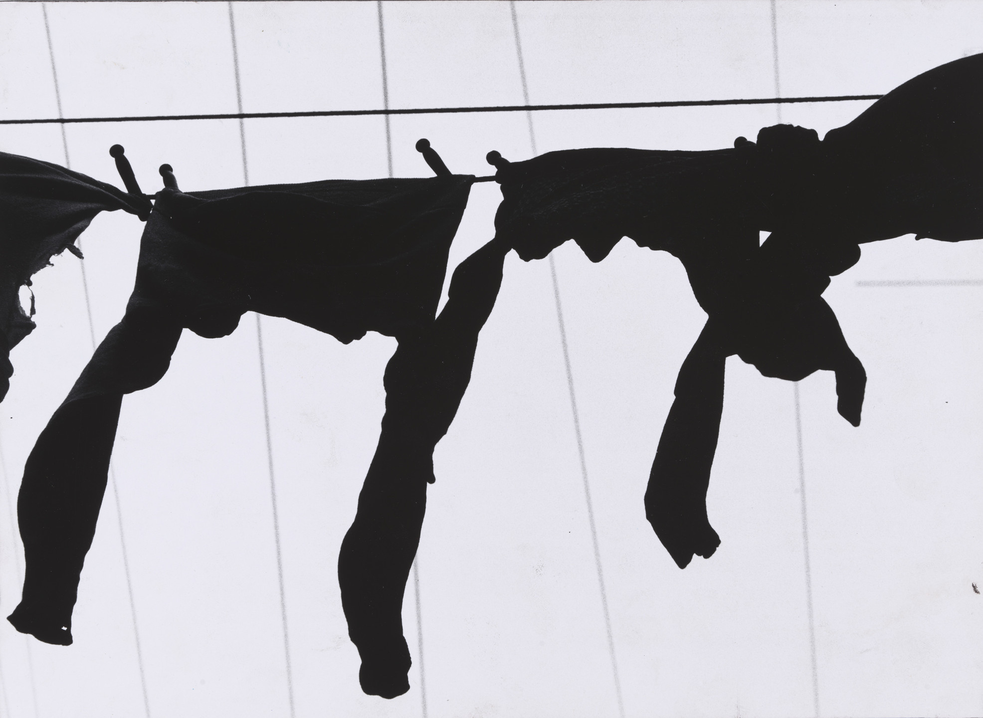 Dark clothes hang on a clothesline with visible clothespins, set against a light background with thin, vertical lines. The predominant colors are black and white. This is an AI generated description. To give feedback, email ai@moma.org.