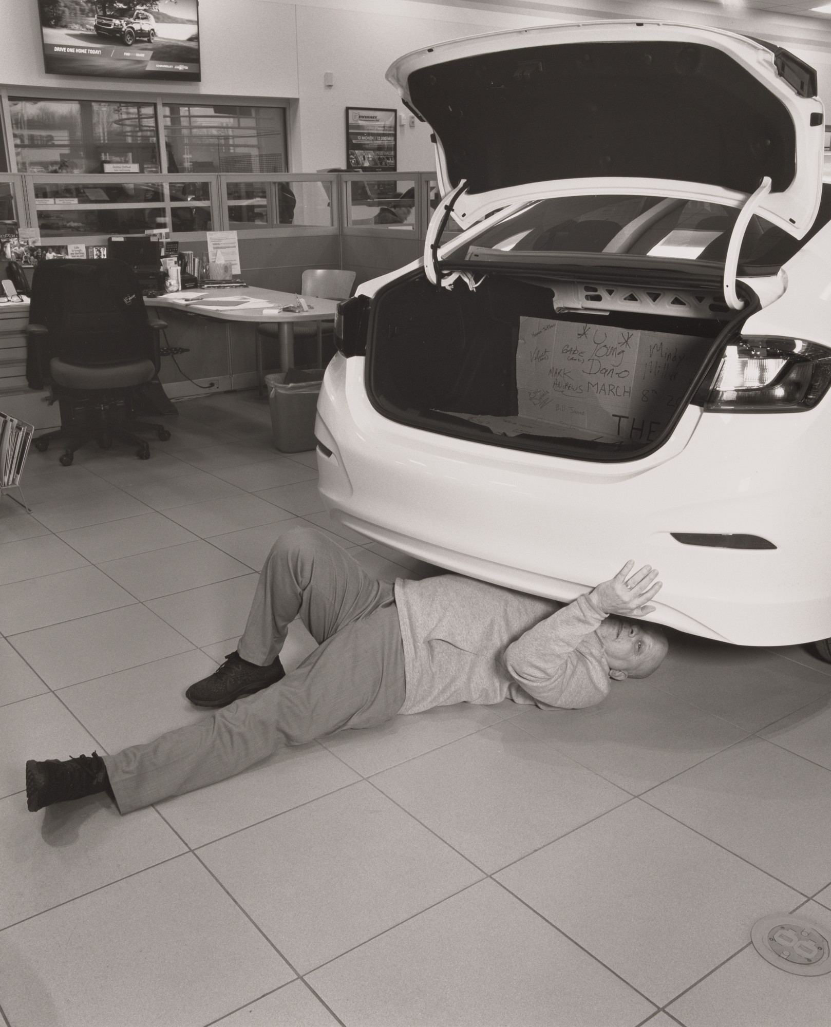 LaToya Ruby Frazier. Keith Burke, Sales and Leasing Specialist, looking for hidden signatures left near the chassis and frame underneath the last Cruze by the United Auto Workers, Sweeney Chevrolet Buick GMC car dealership, Boardman, OH.