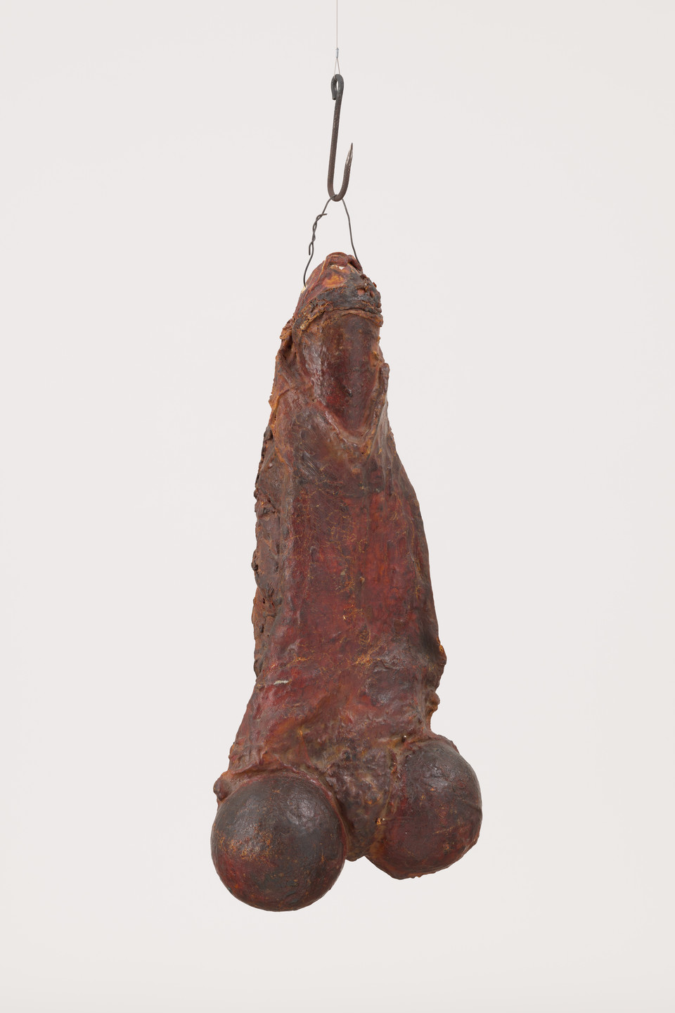 A reddish-brown object resembling a large piece of hanging meat, suspended from a hook. The meat-like form has a textured, aged surface and appears heavy. This is an AI generated description. To give feedback, email ai@moma.org.