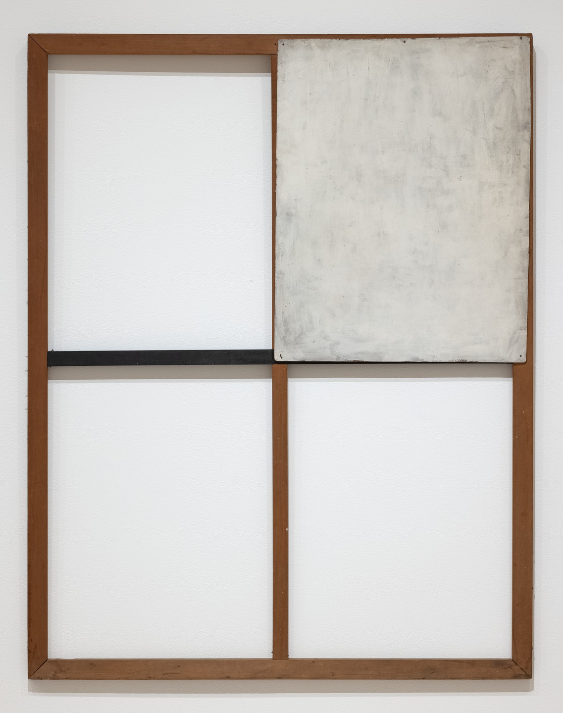 An empty wooden frame is divided into four sections by wooden bars, with a large, faded, white-painted canvas occupying the upper right section, over a black horizontal bar. The background is a plain white wall. This is an AI generated description. To give feedback, email ai@moma.org.