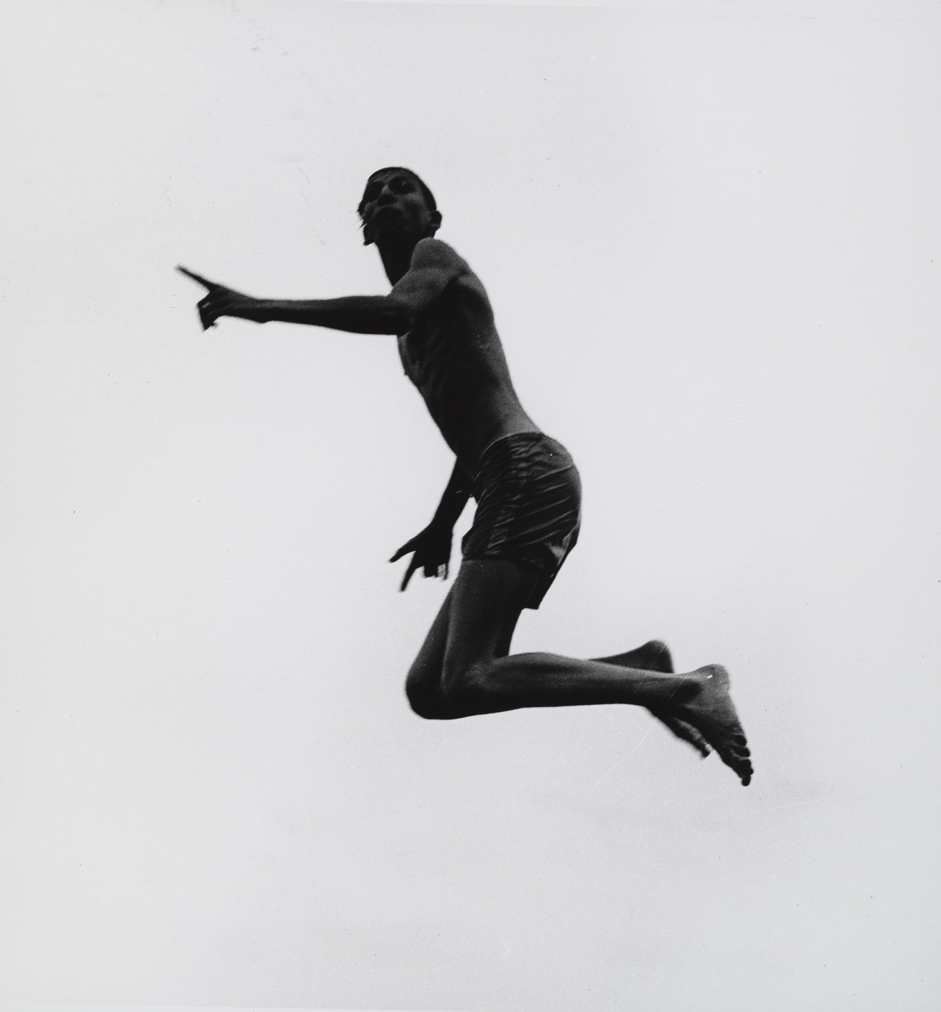 A person in mid-jump with one arm pointing forward, set against a plain white background. The figure is shirtless and wearing shorts, appearing in a black silhouette. This is an AI generated description. To give feedback, email ai@moma.org.