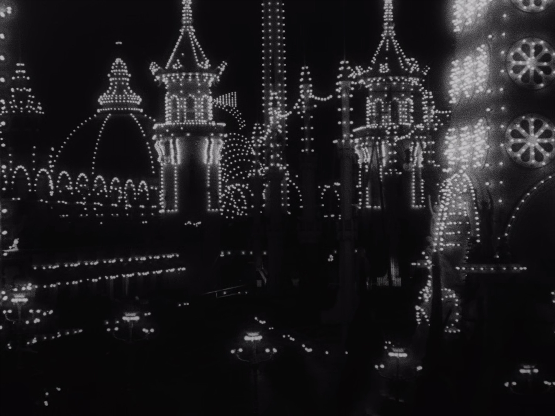 The image depicts a dark scene illuminated by numerous small, bright white lights outlining the shapes of domed and pointed structures. The lights create patterns and arches on tall buildings, with circular light designs visible on the right side. This is an AI generated description. To give feedback, email ai@moma.org.