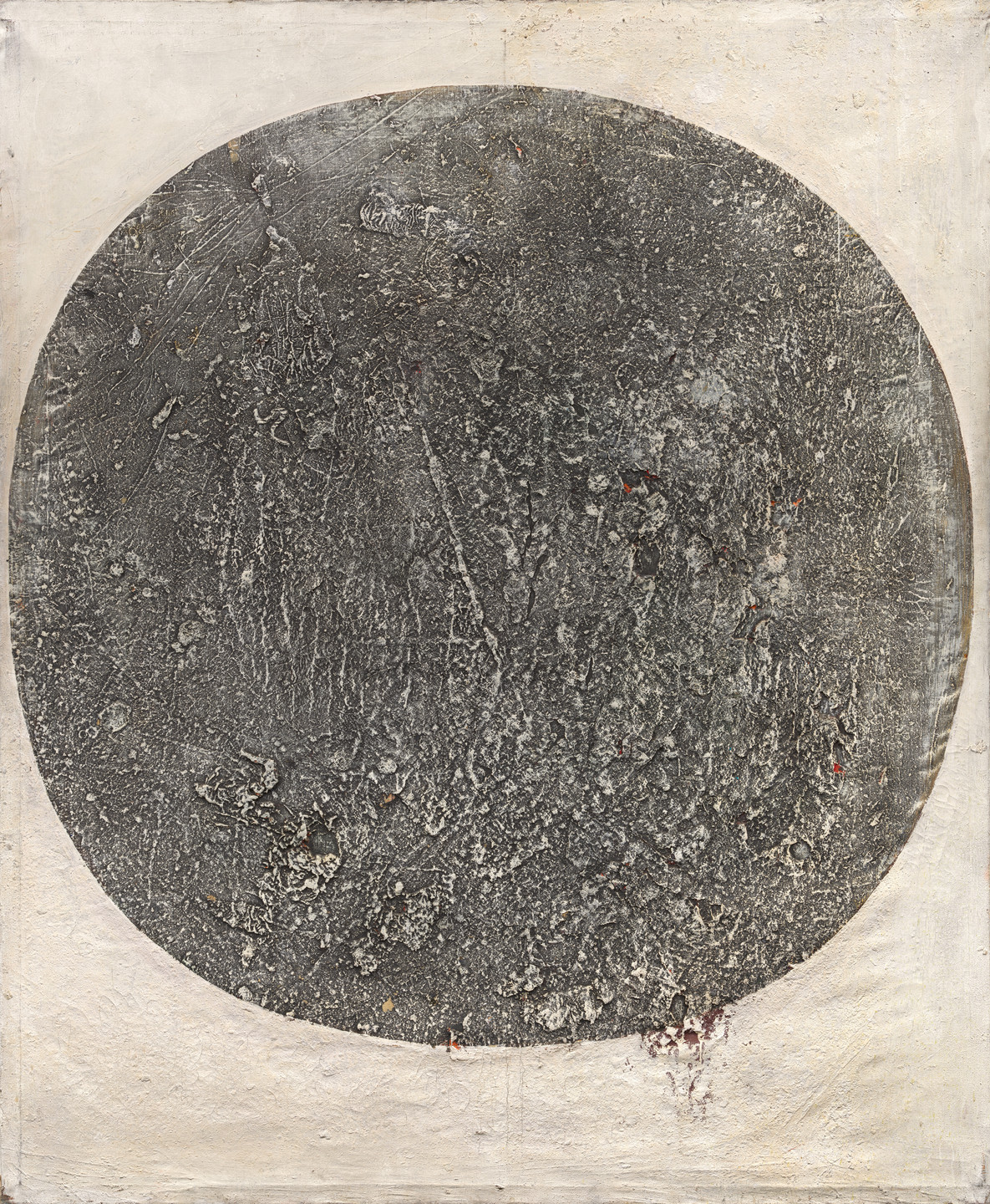 The image shows a large, textured, dark gray circular shape on a light beige background. The circular area contains various rough, uneven surfaces and appears to have minor scattered reddish spots. This is an AI generated description. To give feedback, email ai@moma.org.