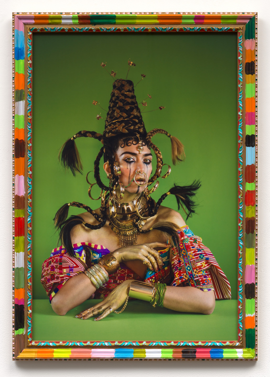 A figure adorned with intricate gold jewelry and elaborate braided hair poses against a vibrant green background. The bright, colorful frame features geometric patterns and multiple shades like red, blue, and yellow. This is an AI generated description. To give feedback, email ai@moma.org.